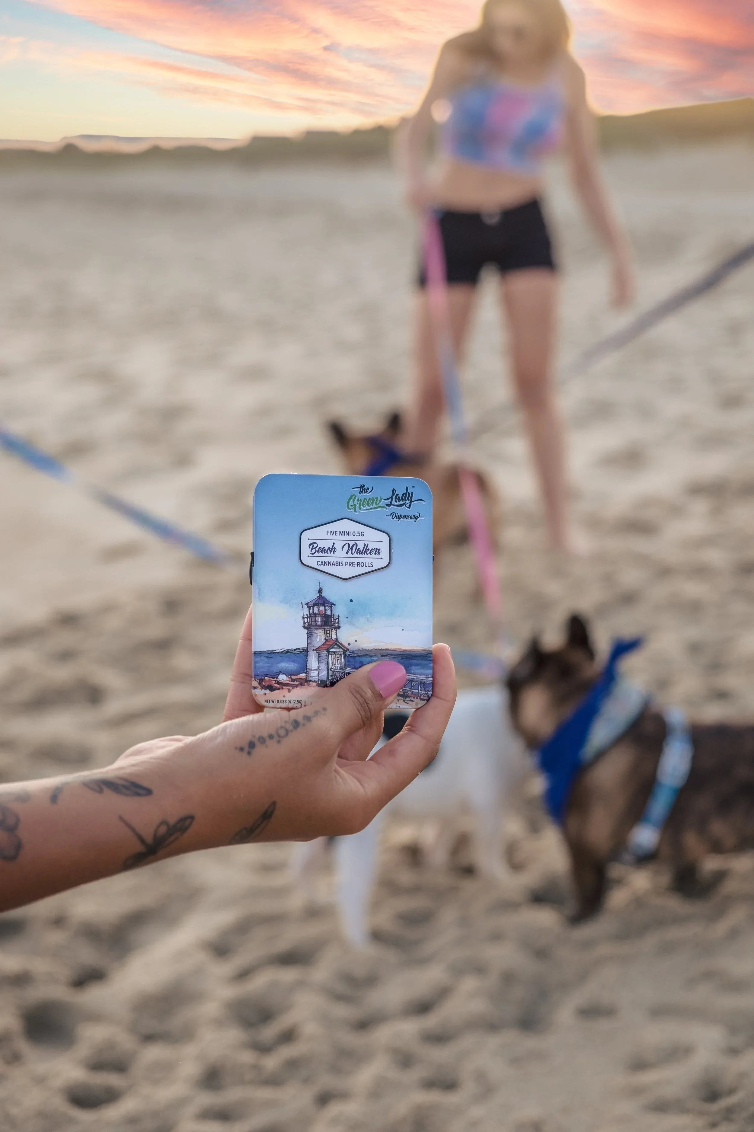 A woman holding a tin of Beach Walkers pre-rolls on the beach with dogs in the background