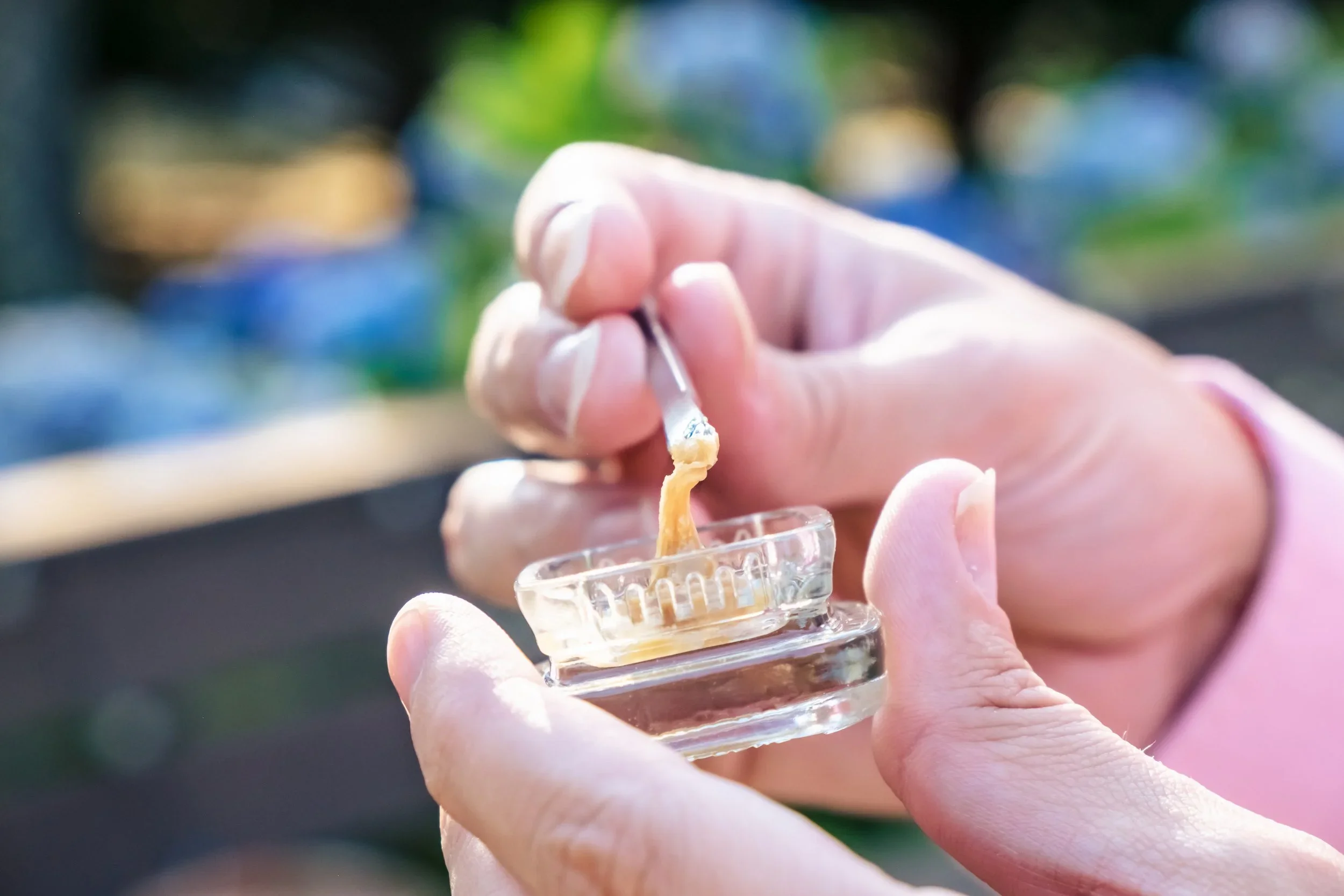 A person's hands holding a small glass container containing a concentrate