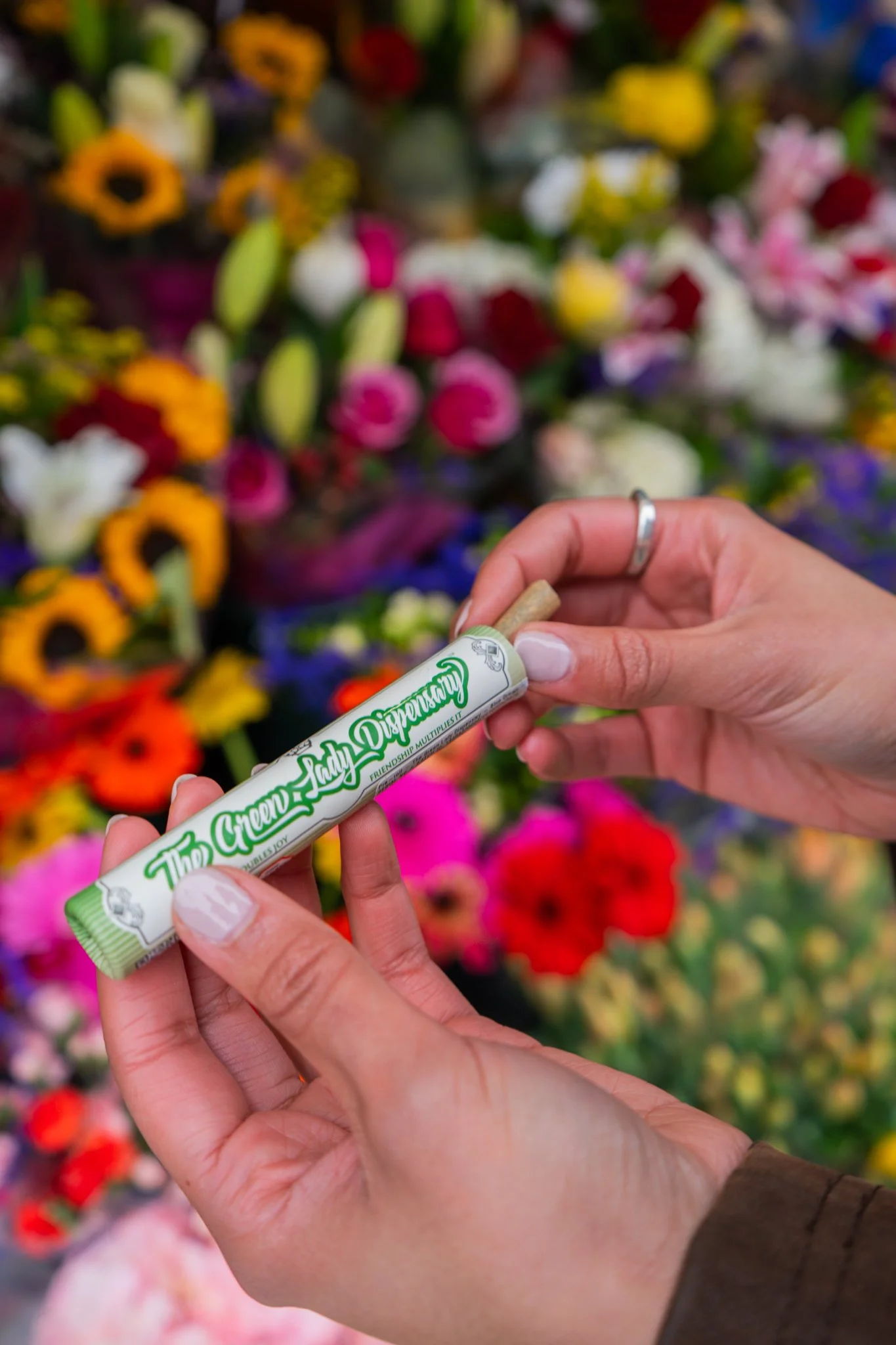 A woman holding a pre-roll from The Green Lady Dispensary with colorful flowers in the background