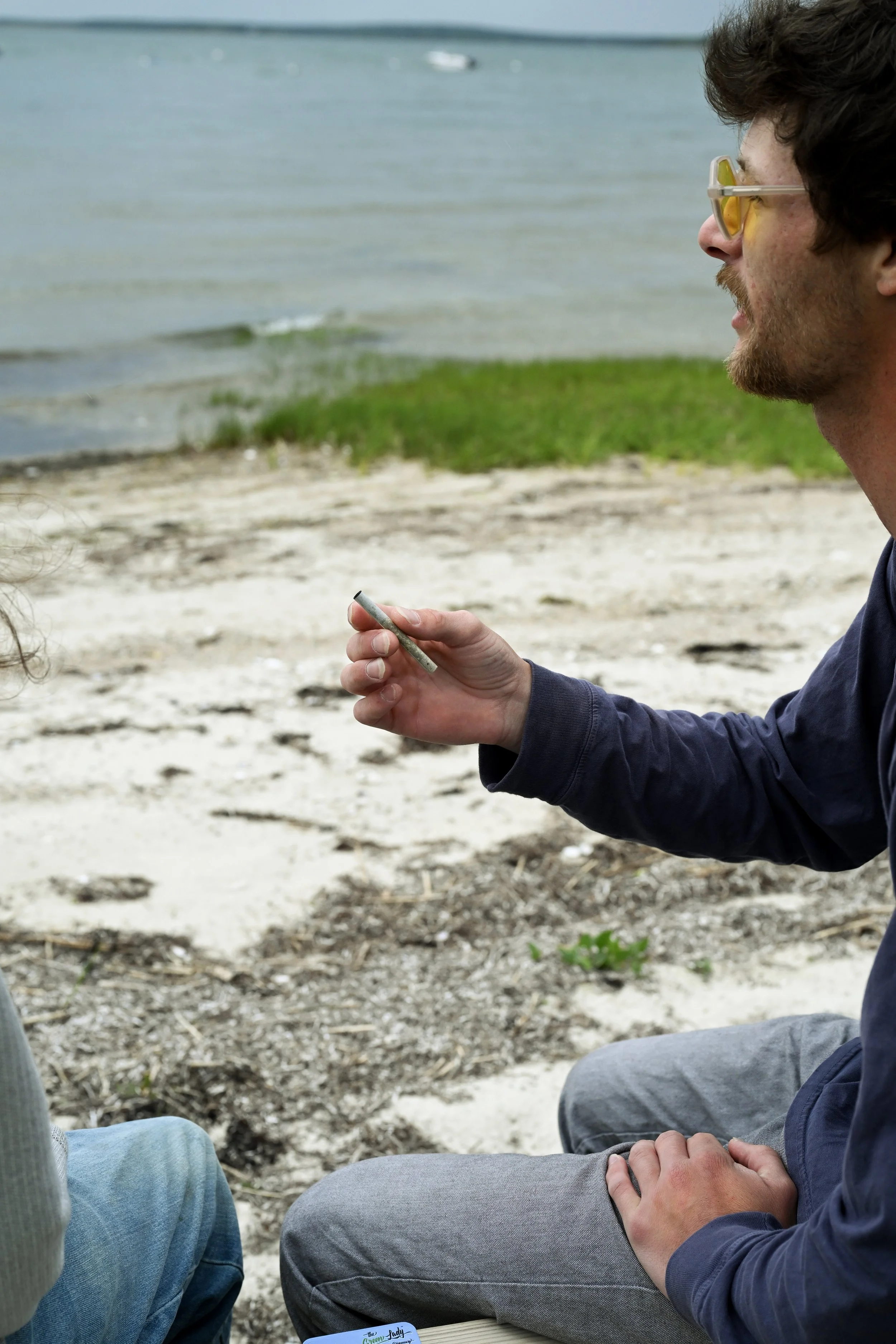 A man sitting on the beach holding a pre-roll from The Green Lady