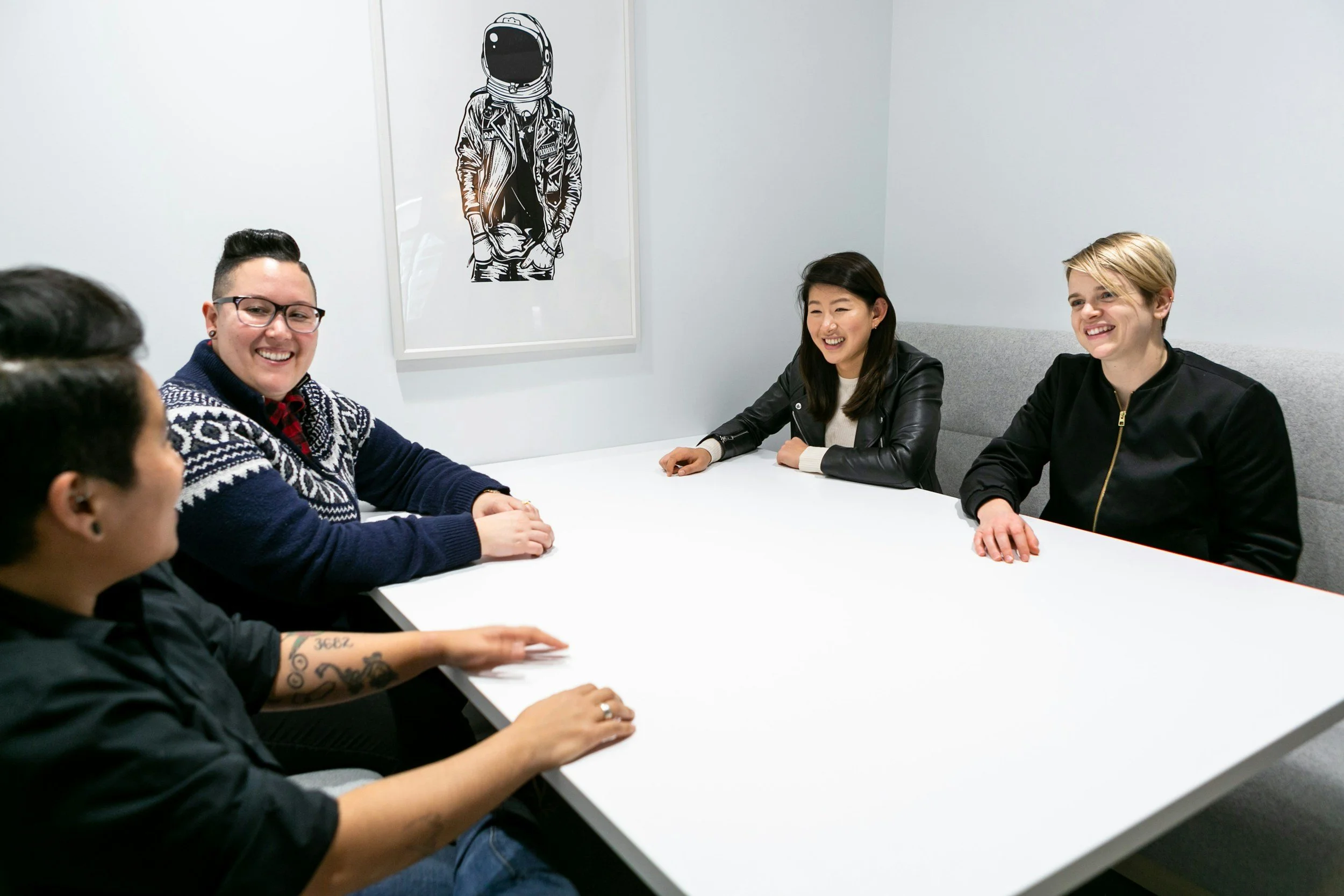 Four people sitting at a white table in a meeting room, smiling and engaging in conversation.