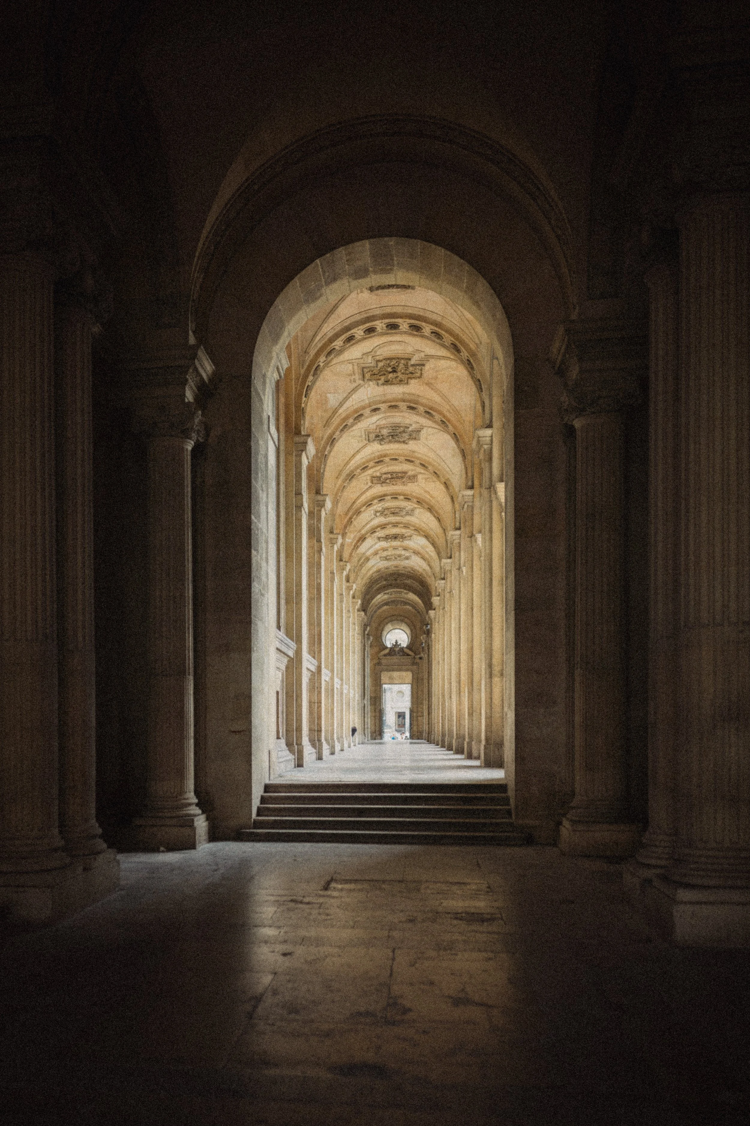 A long corridor with arches and columns, illuminated by natural light at the far end.