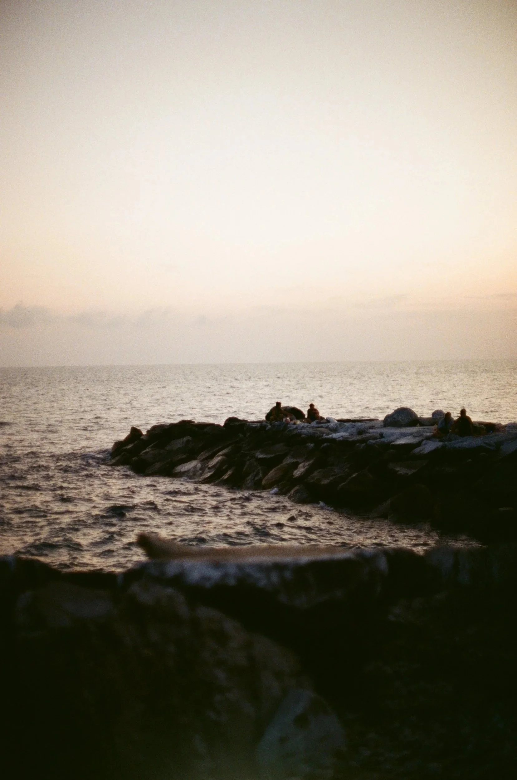 People sitting on rocks by the ocean at sunset.