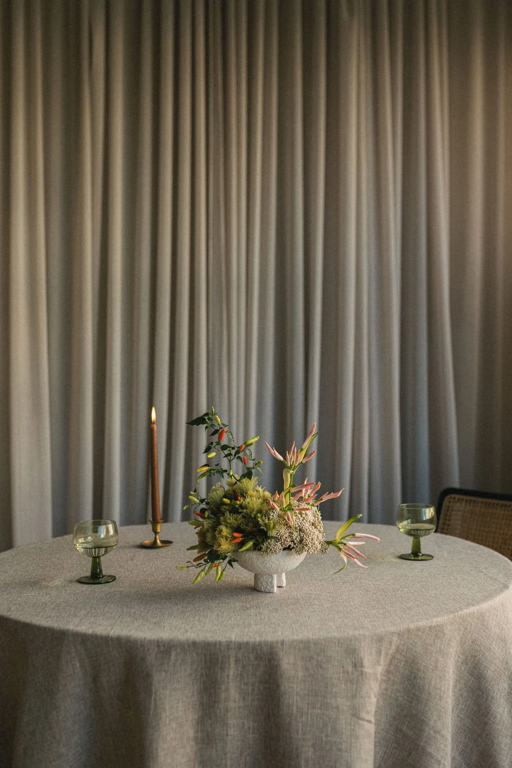 Round linen-draped dinner table with a floral centerpiece, candles and green glassware, tablescape photography Montréal