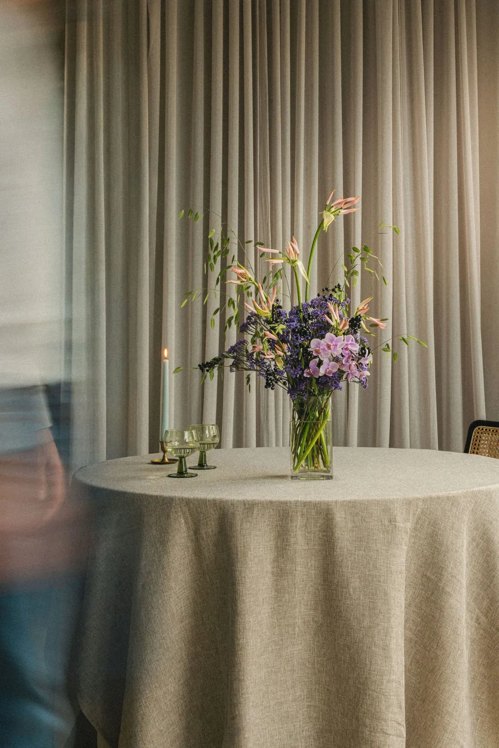 Florist in motion beside a lily and lilac arrangement on a linen table, behind-the-scenes floral photography in Montréal