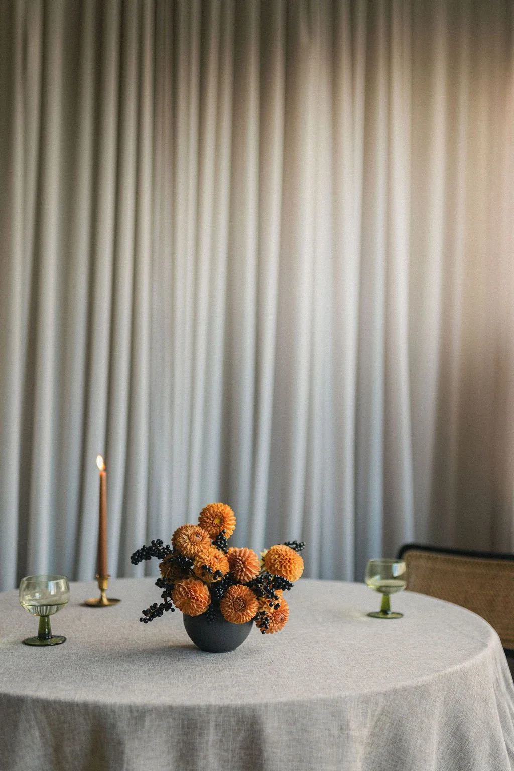 Orange dahlia centerpiece with a taper candle and green glassware on a linen table, event floral photography Montréal