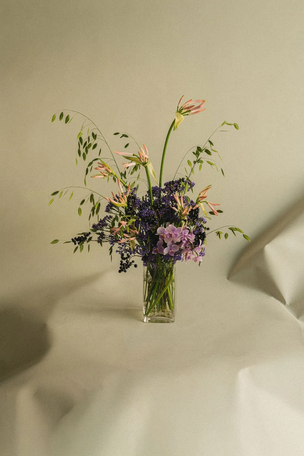 Pink lilies, lilac and wild grasses in a clear glass vase on a linen table, fall floral arrangement by Art et Fleurs, Montréal