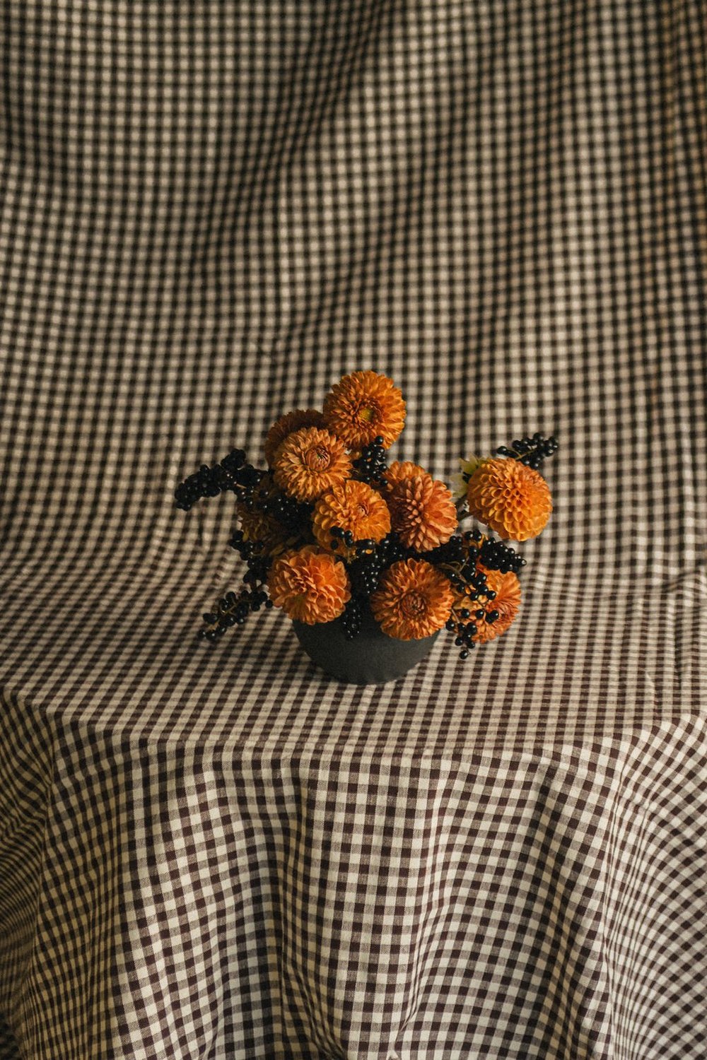 Orange dahlias in a vase on a gingham cloth, still life photography