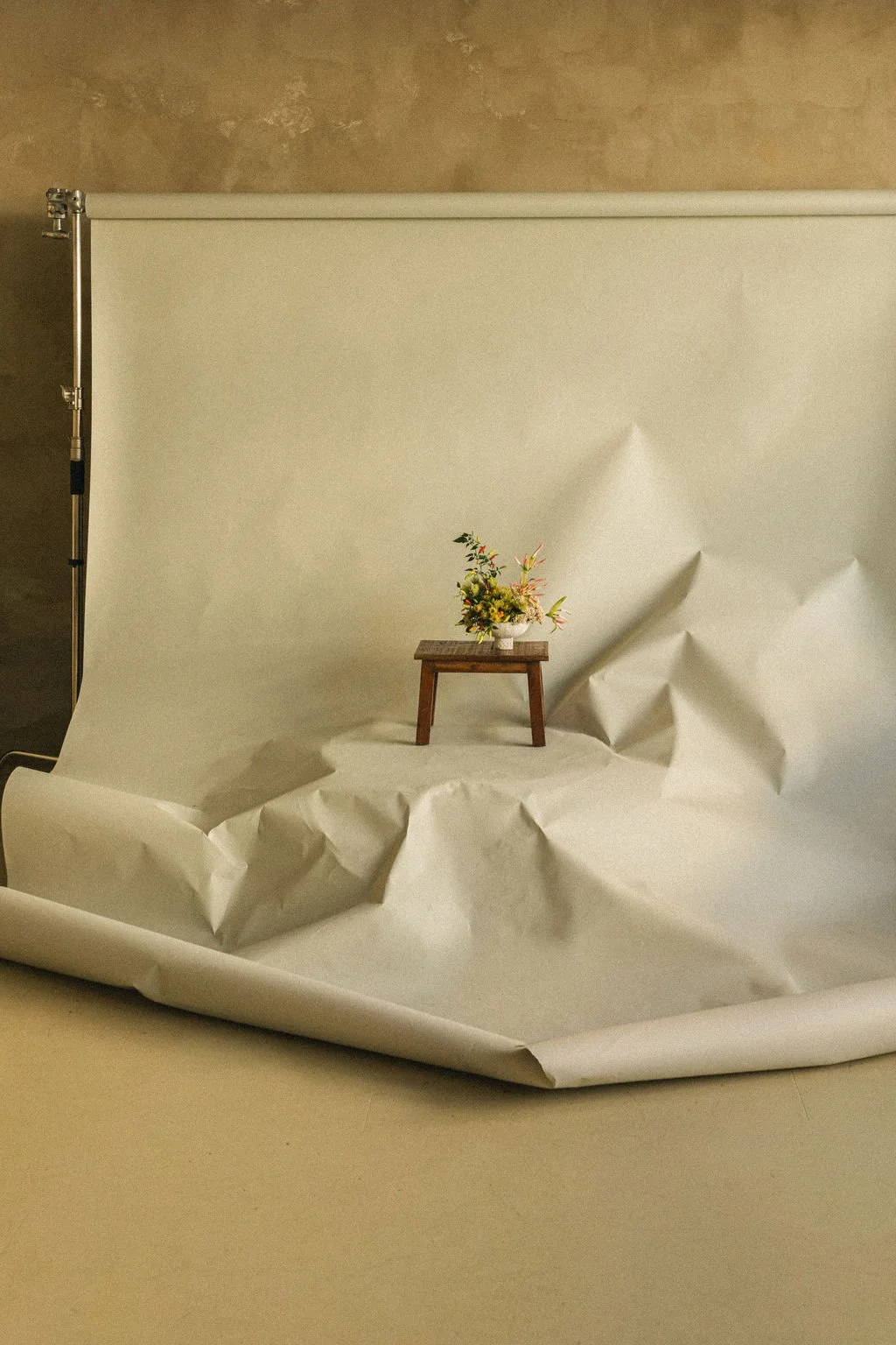 Small fall floral arrangement on a wooden stool in a seamless paper studio set, product photography for a Montréal florist