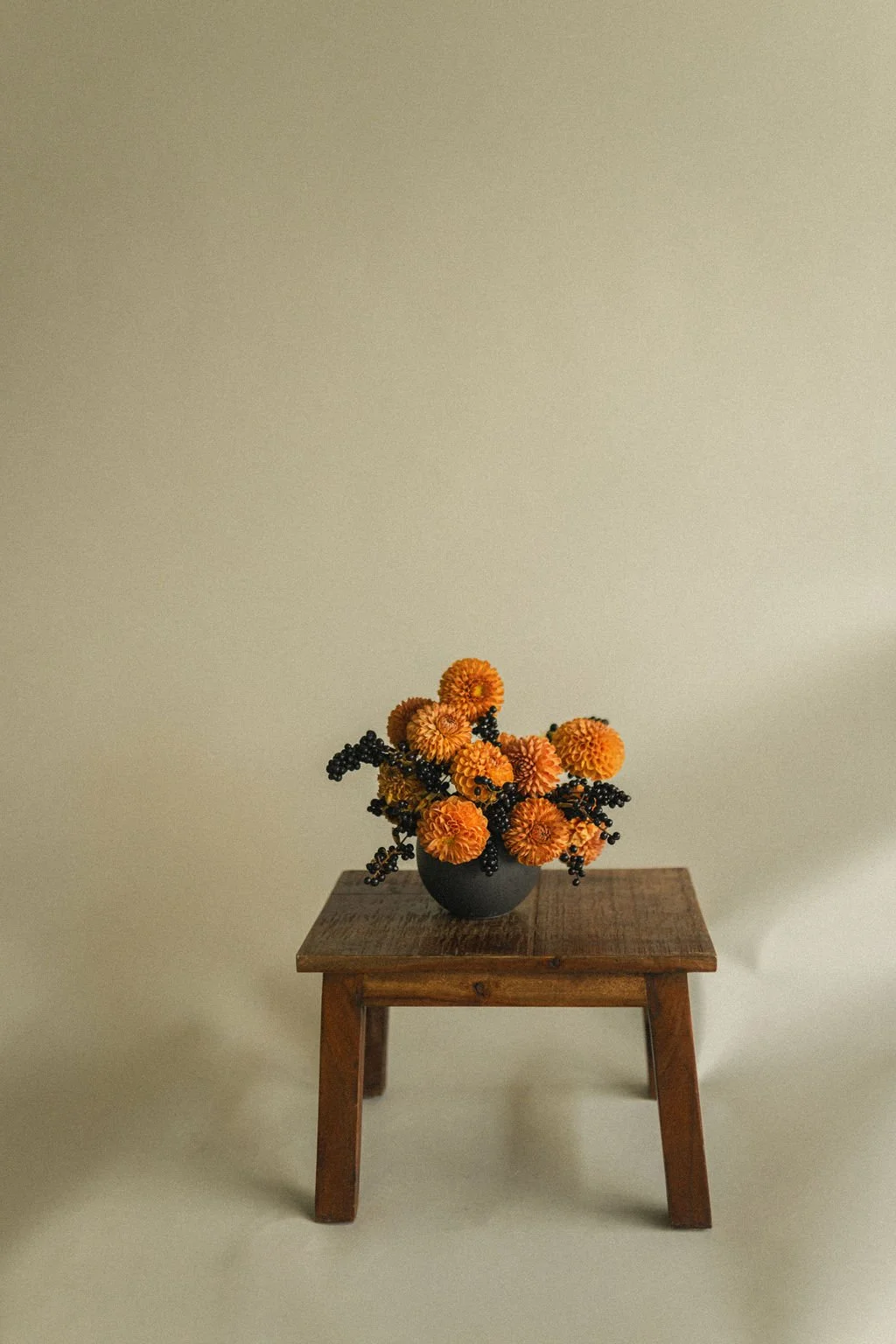 Orange dahlia arrangement in a black vase on a vintage wooden stool, floral photography Montréal for Art et Fleurs