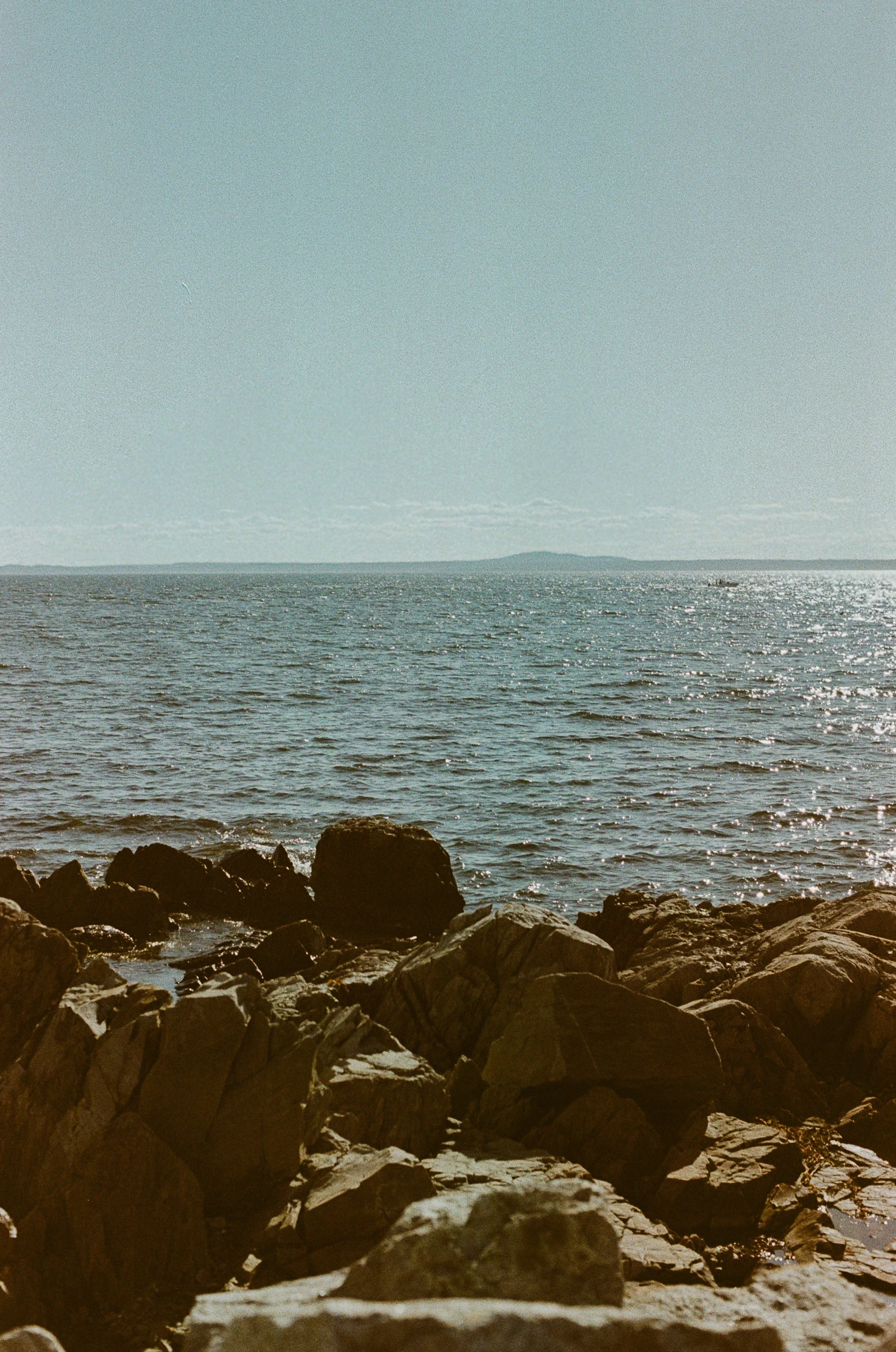 A rocky shoreline with the ocean and distant land in the background, under a partly cloudy sky.