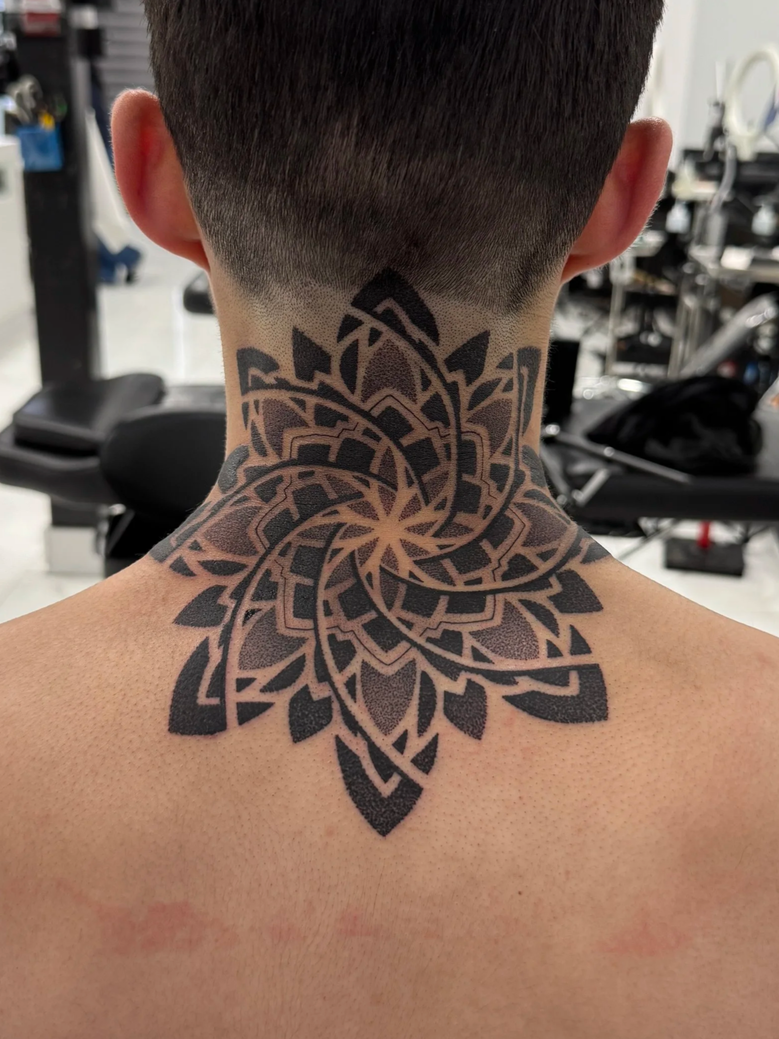 Back of a person's neck with a large, intricate black tattoo featuring geometric and floral patterns.