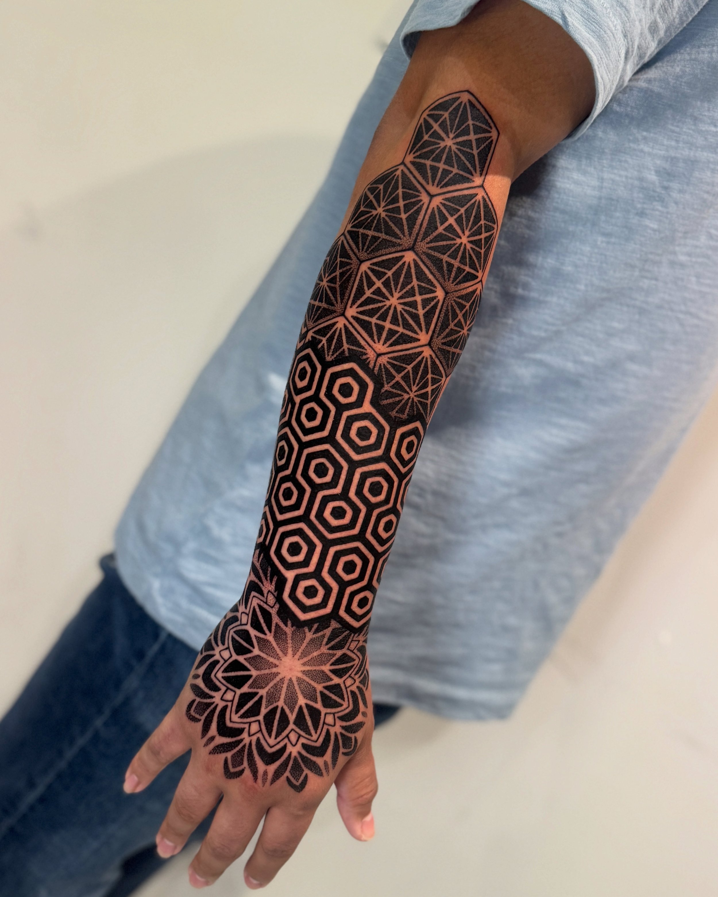 Close-up of a person's arm with a geometric black and pink tattoo featuring interconnected hexagons and starburst patterns.