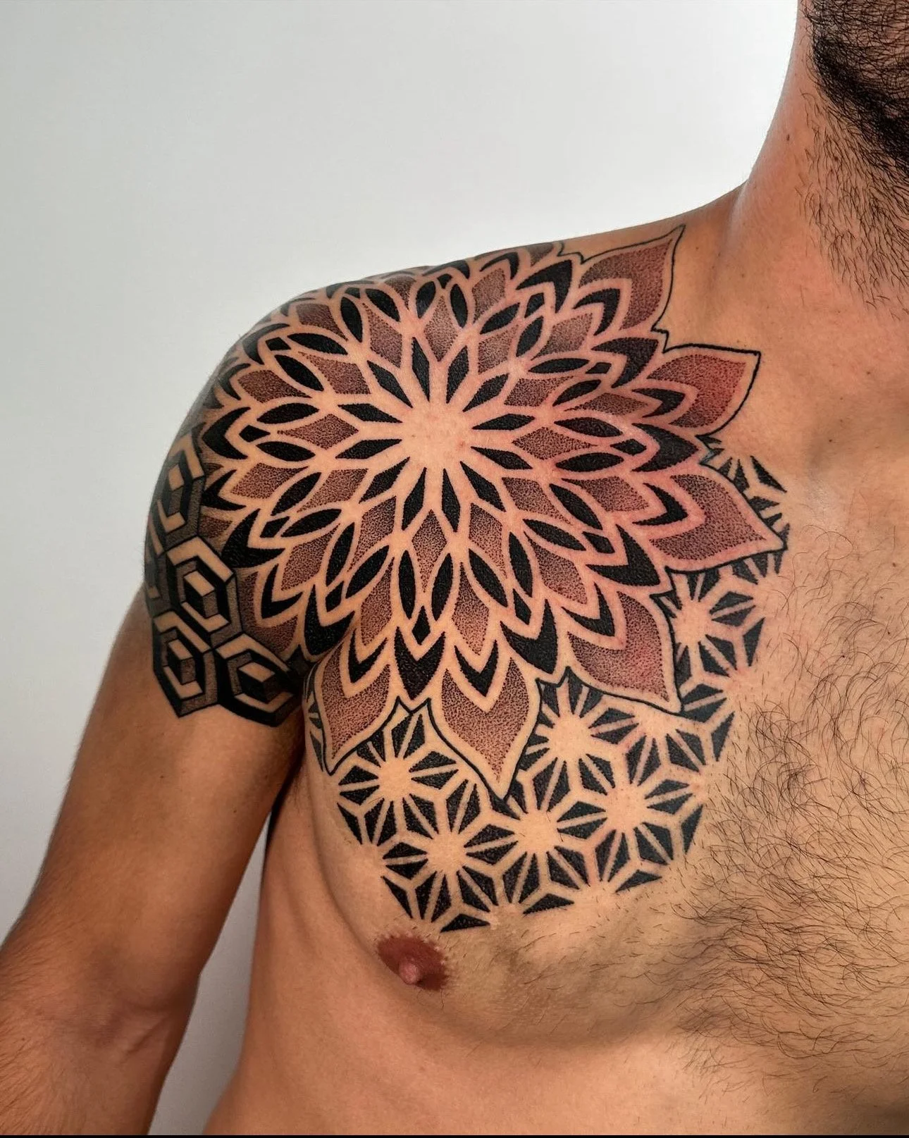 Close-up of a man's upper chest and shoulder with a detailed geometric and floral black ink tattoo.