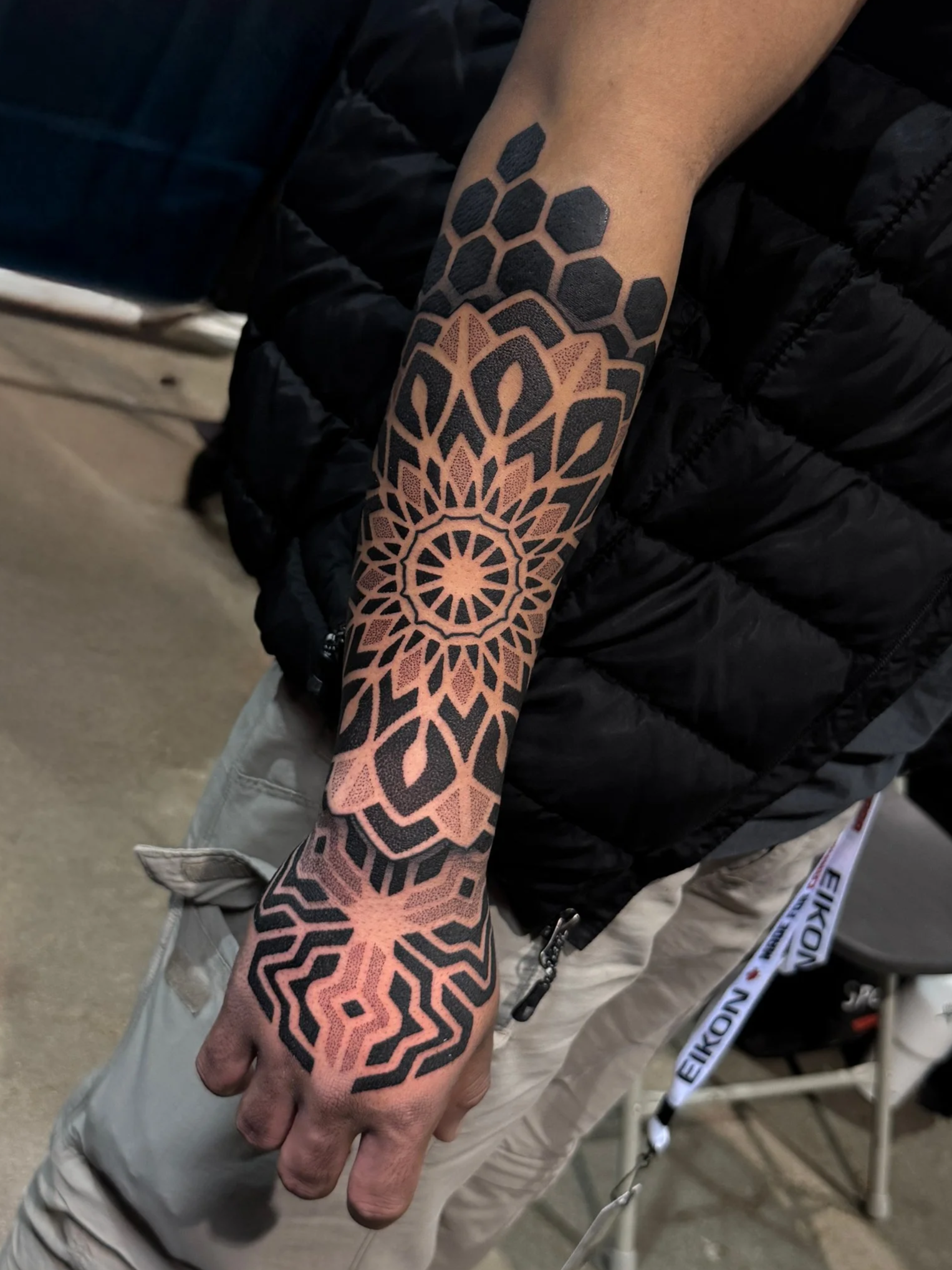 A person's arm with a geometric tattoo design featuring black and pink patterns extending from the wrist to the elbow.