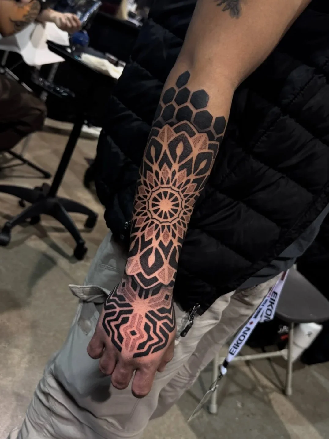 A person's arm with a tribal-style tattoo featuring geometric patterns including honeycomb shapes and radiating lines.