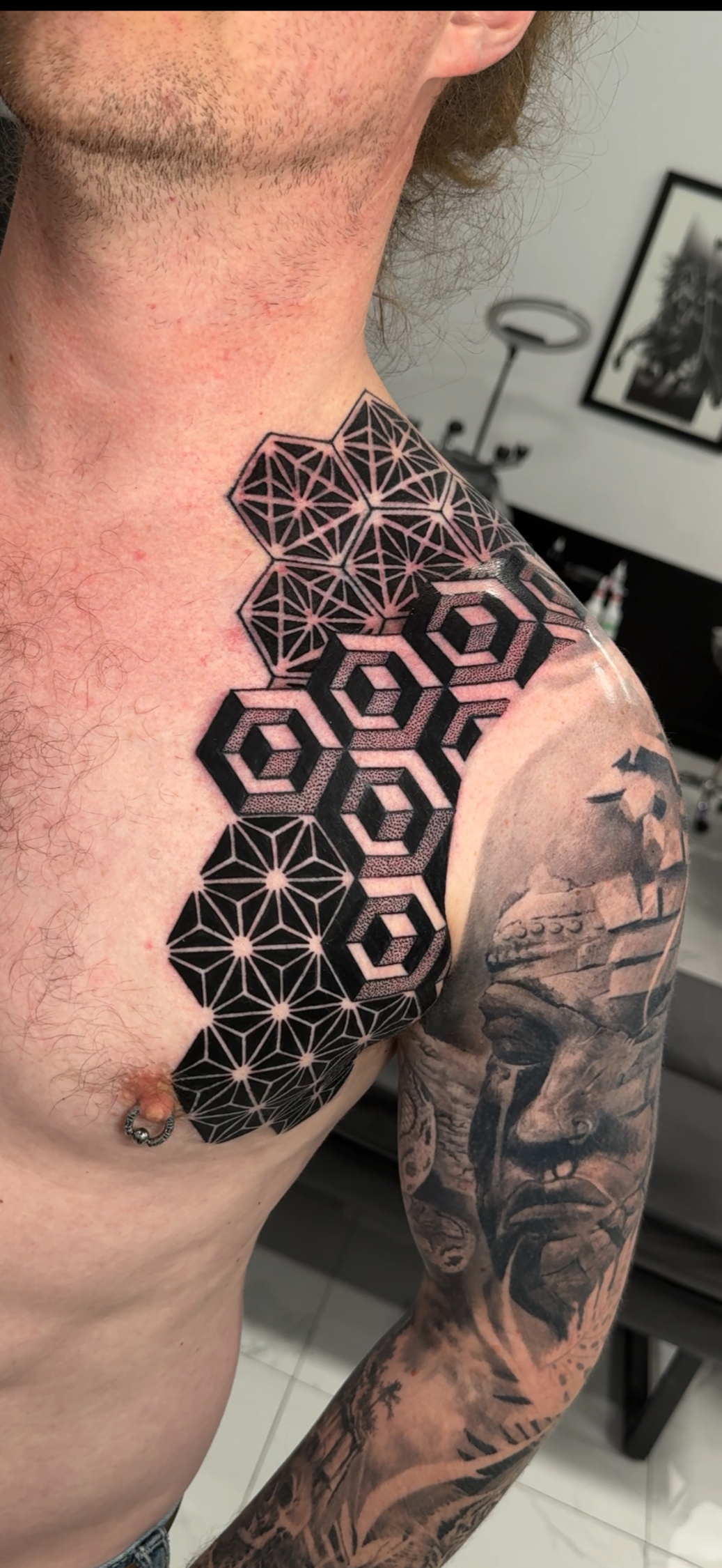Tattoo on person's chest and shoulder featuring geometric patterns with interconnected hexagons and star-like shapes in black ink.