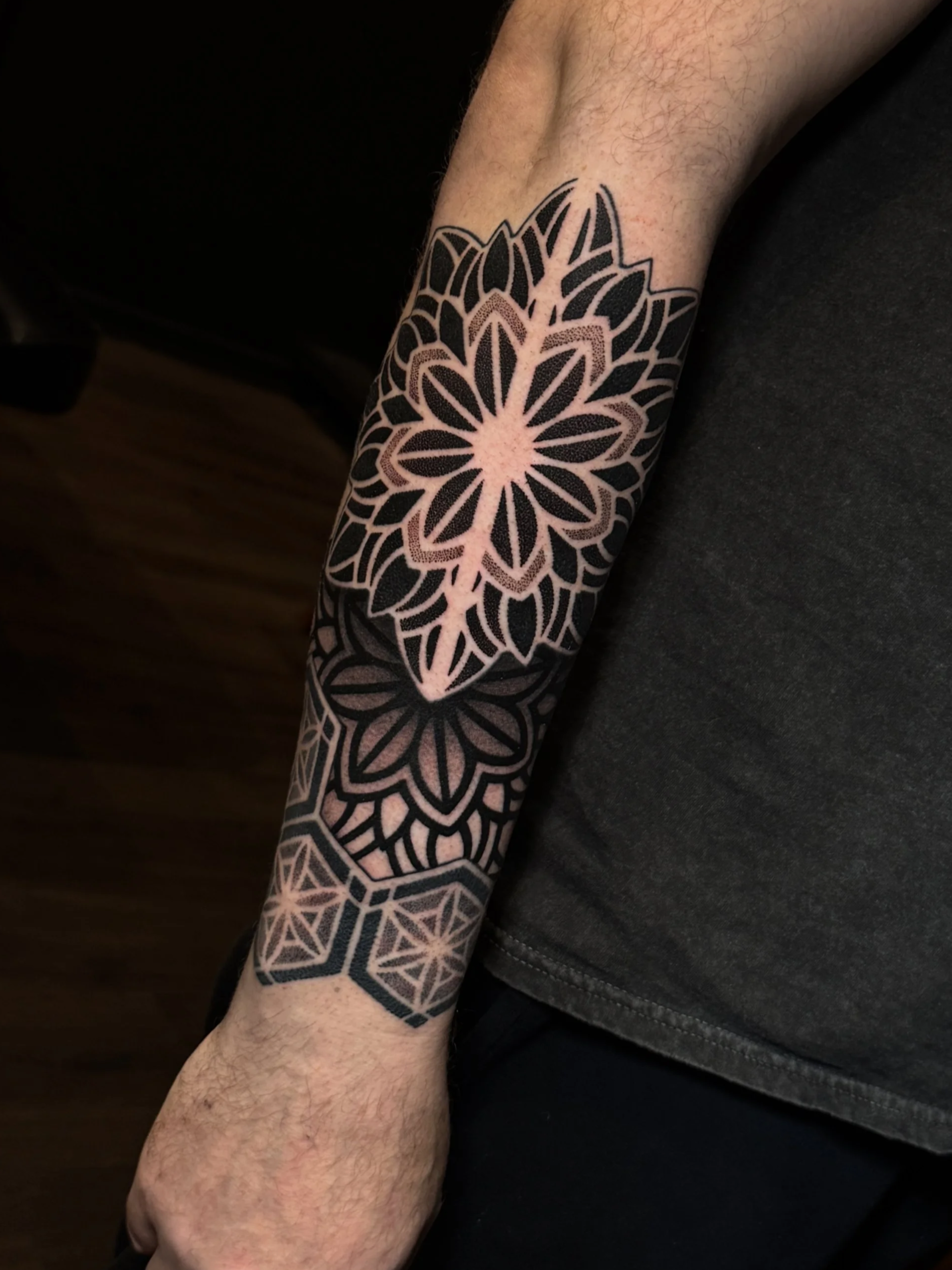 A person's arm with a geometric tattoo consisting of a large floral pattern with black and brown ink.