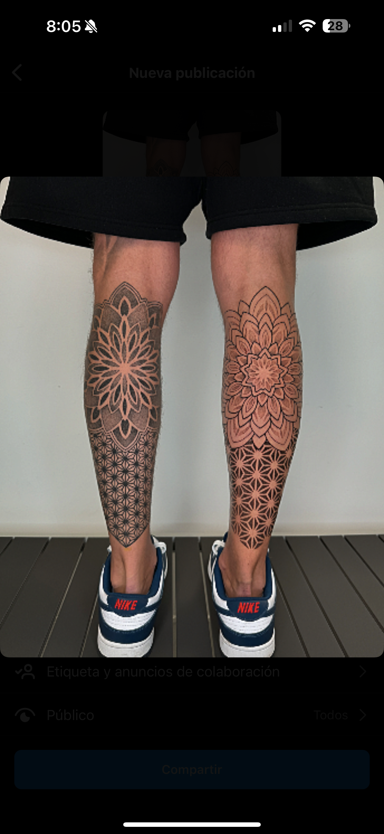 Person standing on a wooden floor, wearing black shorts, white and black Nike sneakers, with colorful geometric and floral tattoos on both legs.