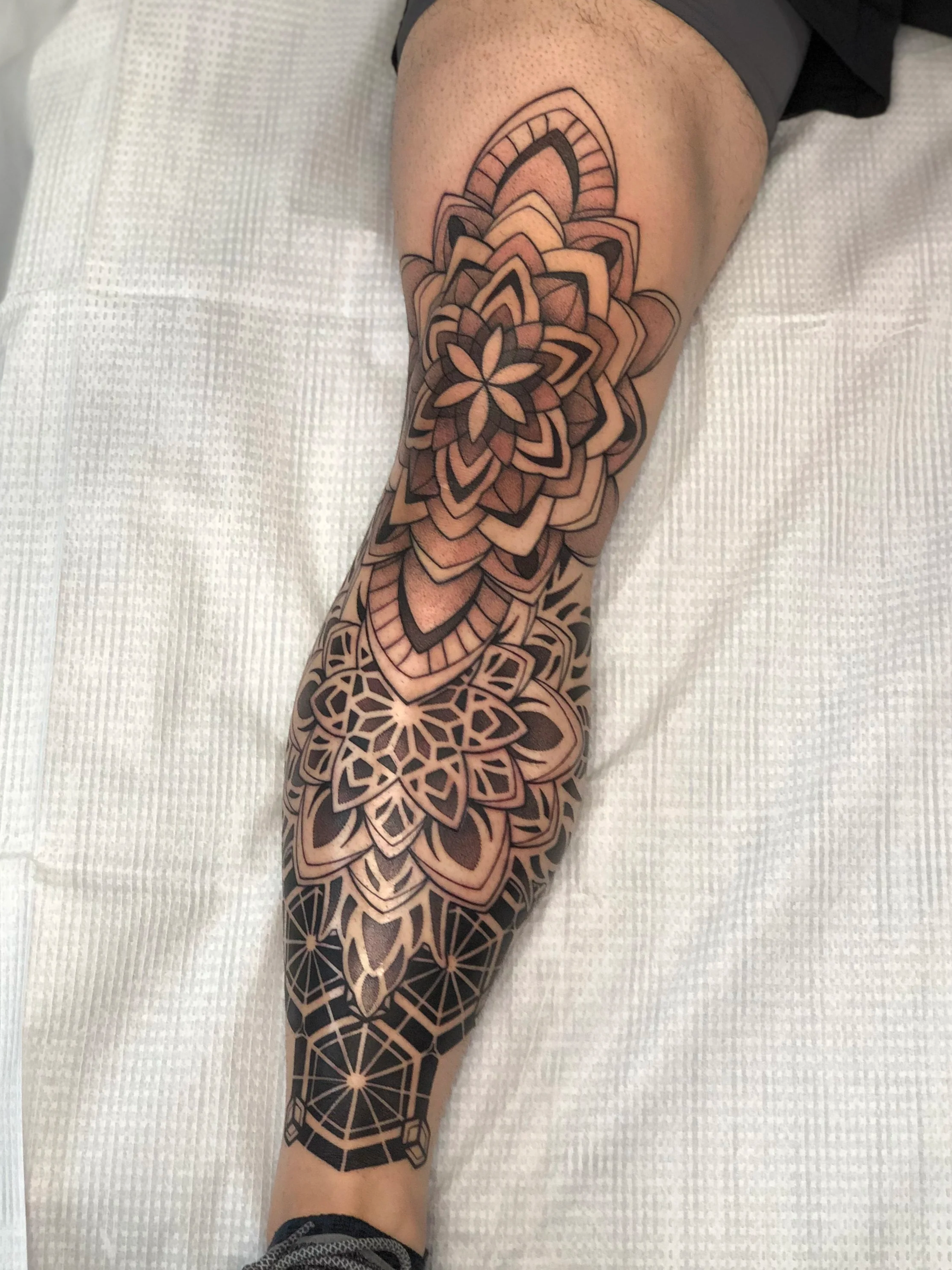 A tattoo sleeve on a person's arm featuring bold, black geometric patterns, floral designs, and intricate linework.