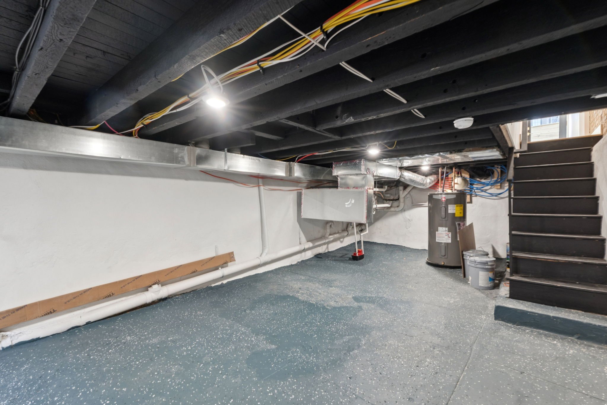  unfinished basement with exposed ceiling beams, electrical wires, and ducts, with some construction materials and stairway to upper level