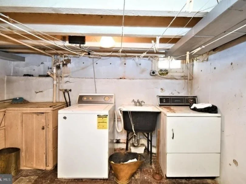 Laundry area with washer and dryer, utility sink, wooden cabinet, and exposed pipes in a basement.