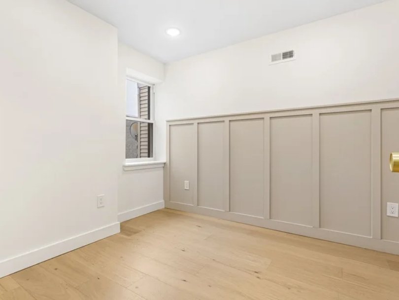 Empty room with beige paneled wall, small window, and hardwood floor.