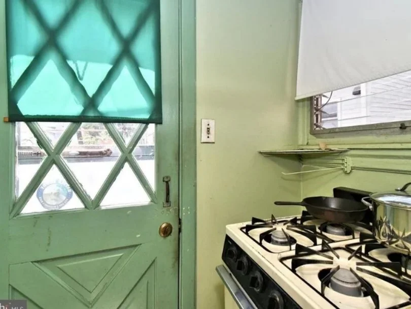 Interior of a kitchen with a light green door and wall, a window with a blind, and a white stove with pots and pans.