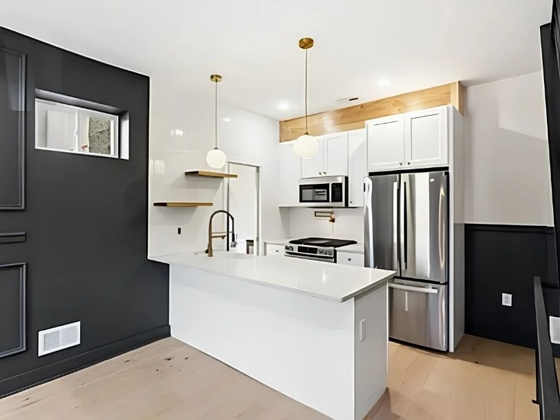 Modern kitchen with white cabinets, stainless steel refrigerator, black stove, microwave, pendant lights, and wooden accents, with a white countertop and black and white walls.