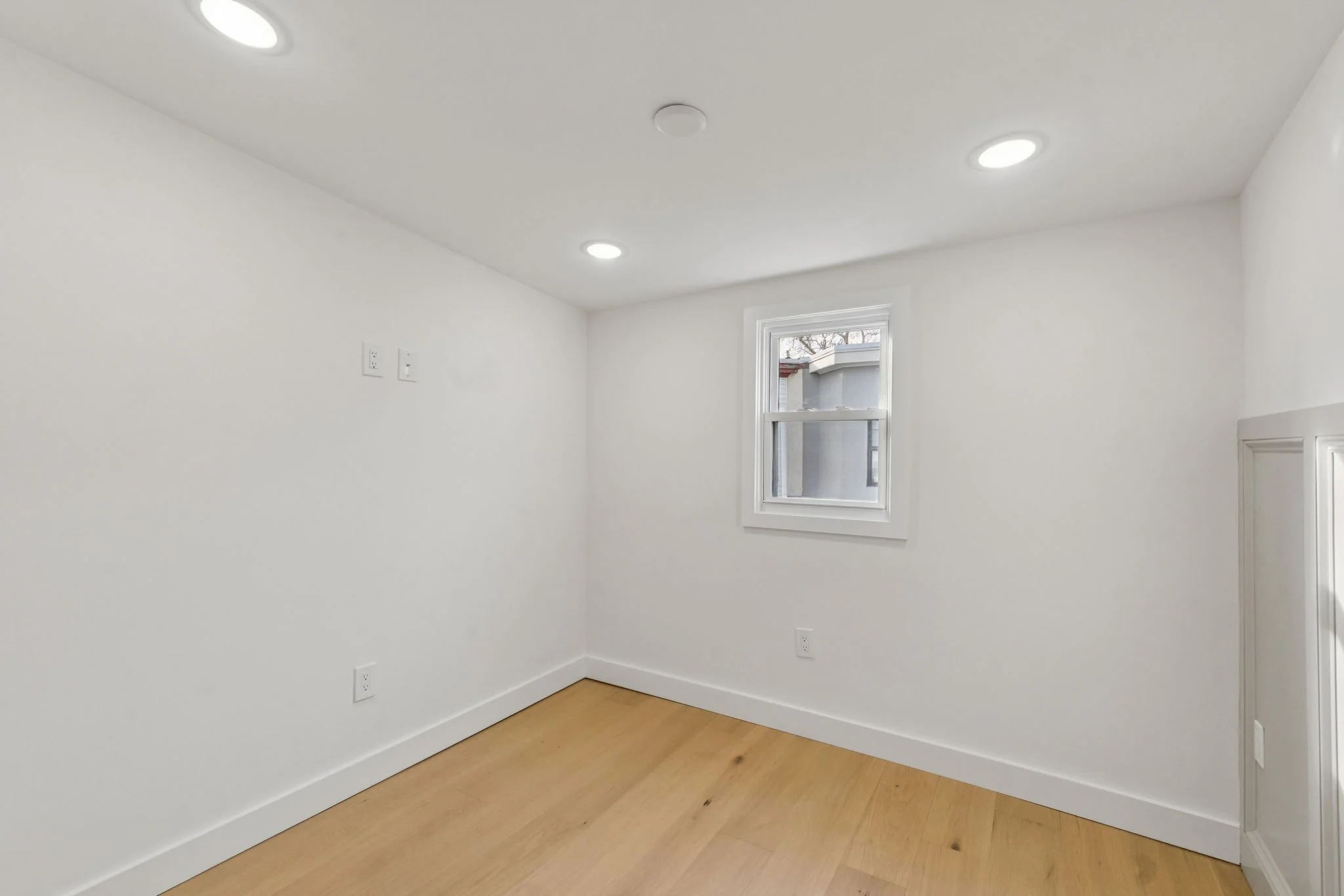 Empty white room with wood floor, a window, and ceiling lights.