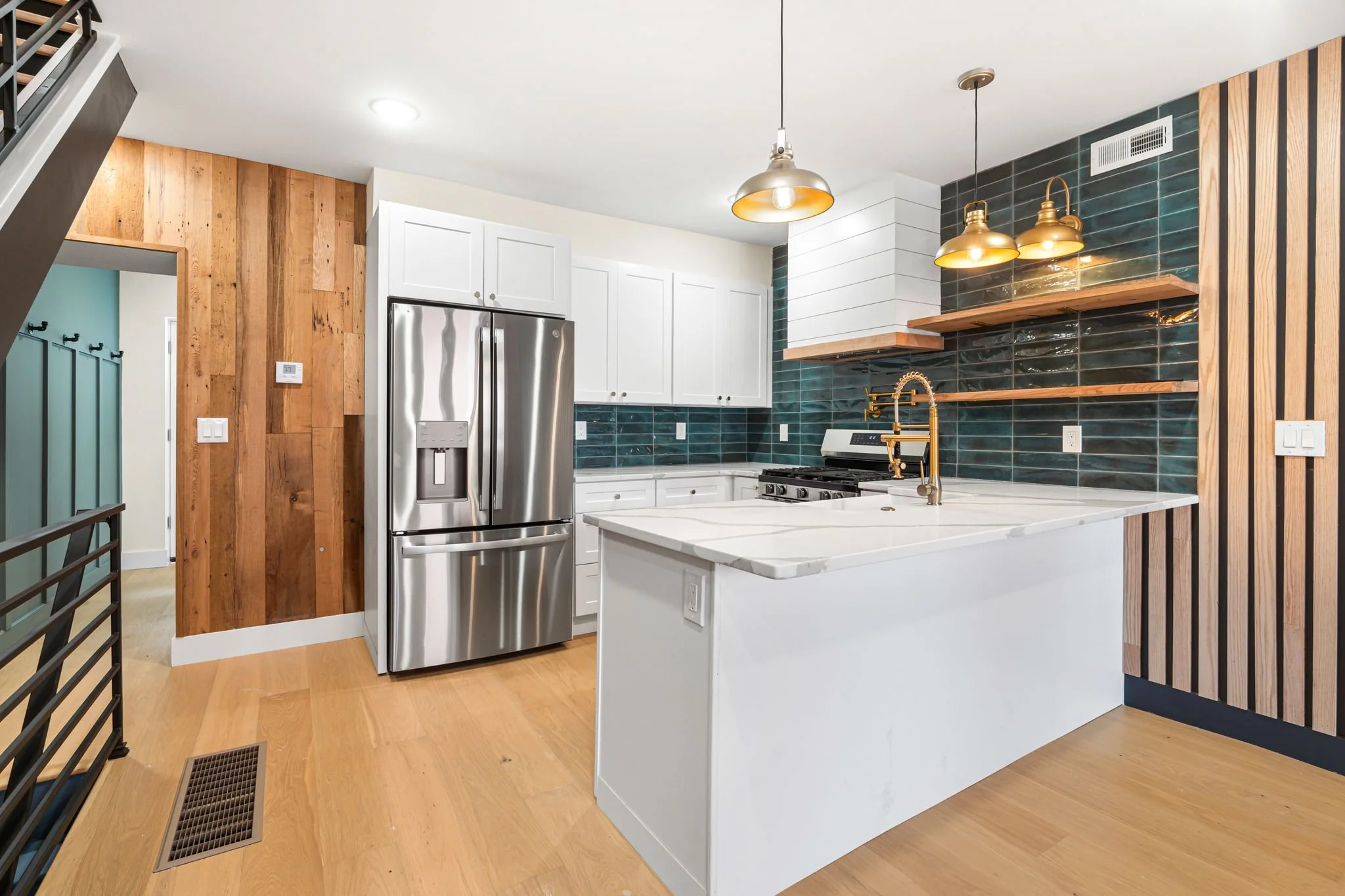 Modern kitchen with white cabinets, stainless steel refrigerator, blue tiled backsplash, and wooden accents, illuminated by pendant lights.