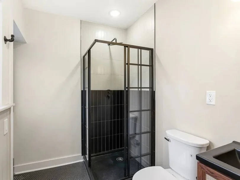 Small bathroom with a black glass shower enclosure, white walls, a white toilet, and a wooden vanity with a black countertop.