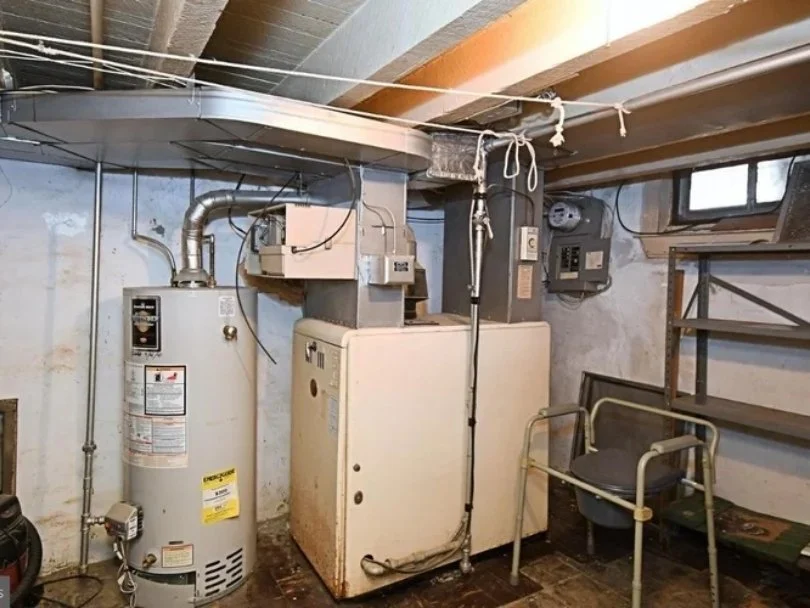 A water heater and an older washing machine in a basement with concrete walls, wiring, and shelving.