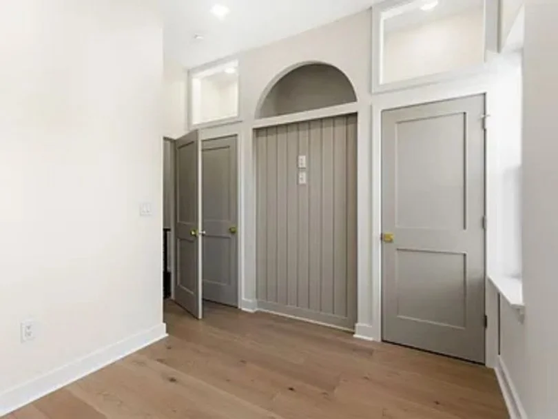 Empty room with white walls, light wood flooring, and gray doors and paneling, including a curved top panel and rectangular panels.
