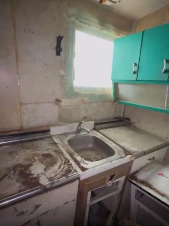 Dirty, worn kitchen sink area with mold and grime, old cabinetry, and a small window.