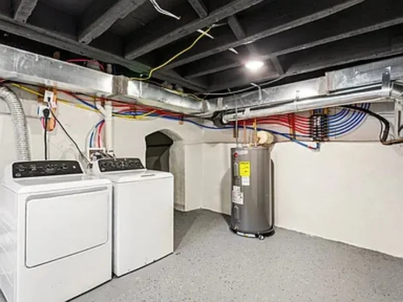 Basement laundry room with a washing machine, dryer, and a water heater along with exposed pipes and wiring on ceiling and wall.