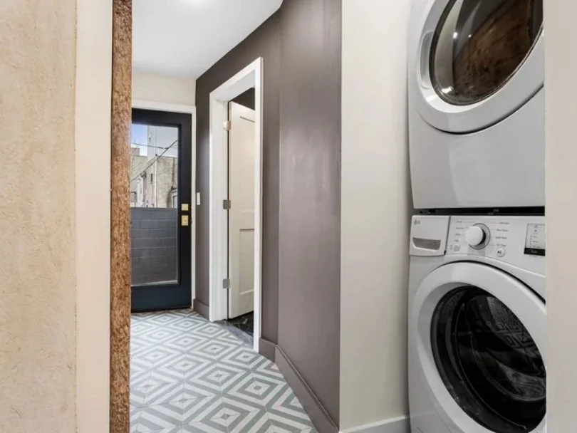 Laundry area with stacked washer and dryer units next to a hallway, with a door leading outside.