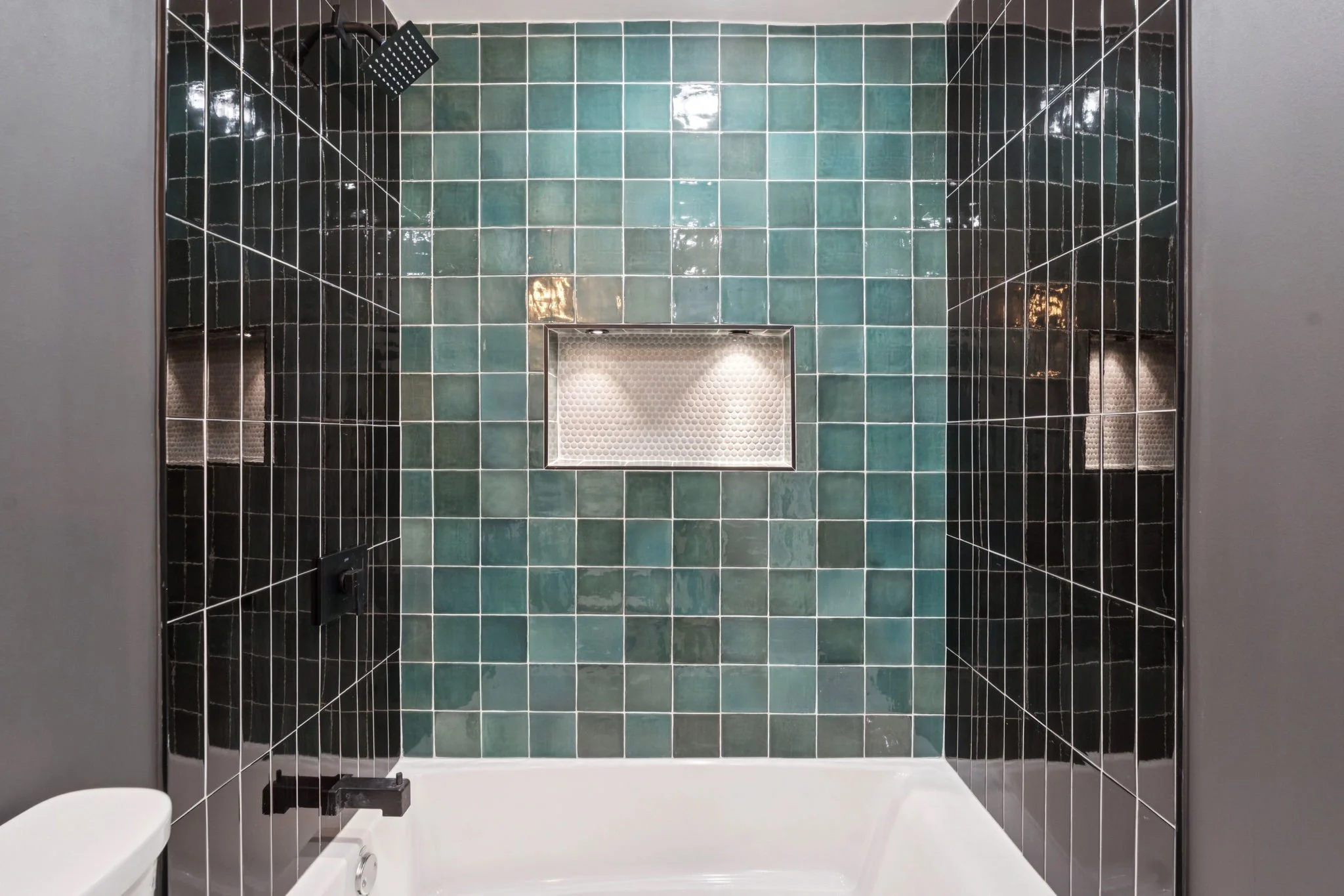 A modern shower with black square tiles on the walls and a center drain, viewed from inside the shower facing towards the back wall.