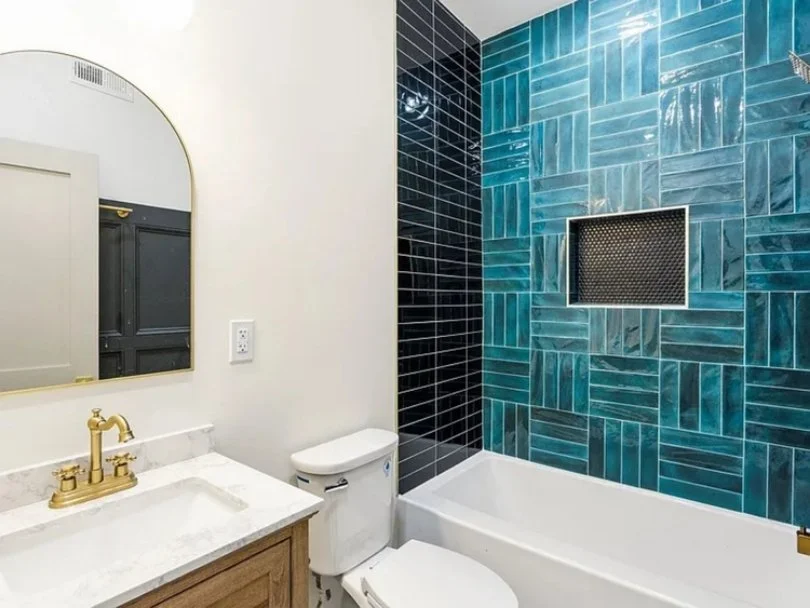 Bathroom with white walls, gold faucet, and a marble countertop sink. Blue tile shower area with a small built-in niche and black tile accents.