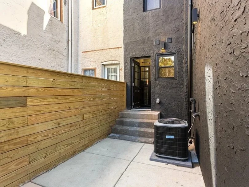 Back entrance with concrete stairs, black door, and an air conditioning unit outside.