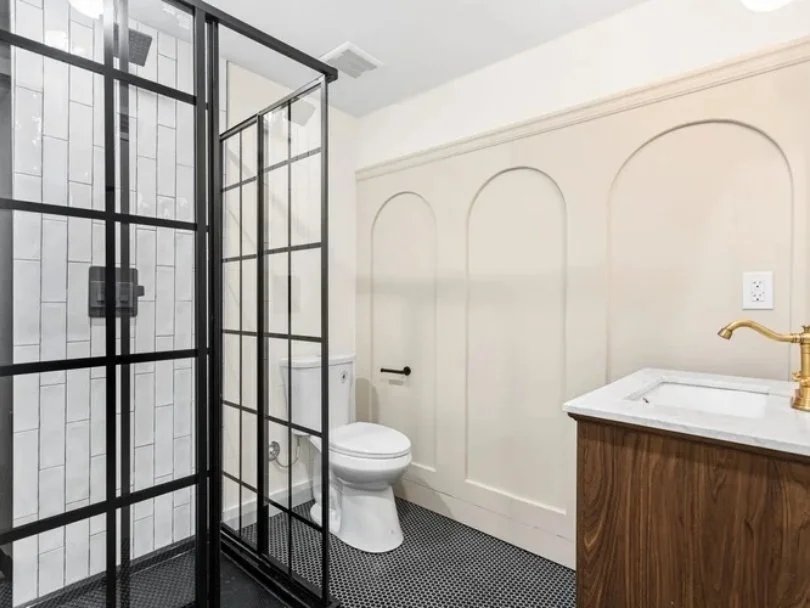 Bathroom with a glass shower enclosure, a white toilet, and a wooden vanity with a white sink and gold faucet.