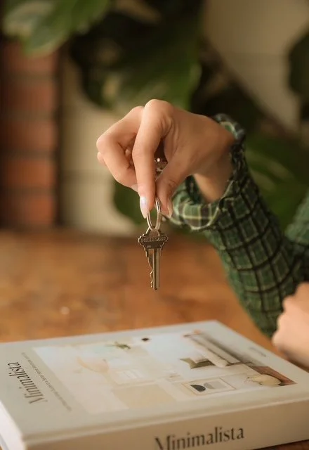 A person holding a key over a magazine on a wooden table with indoor plants in the background.