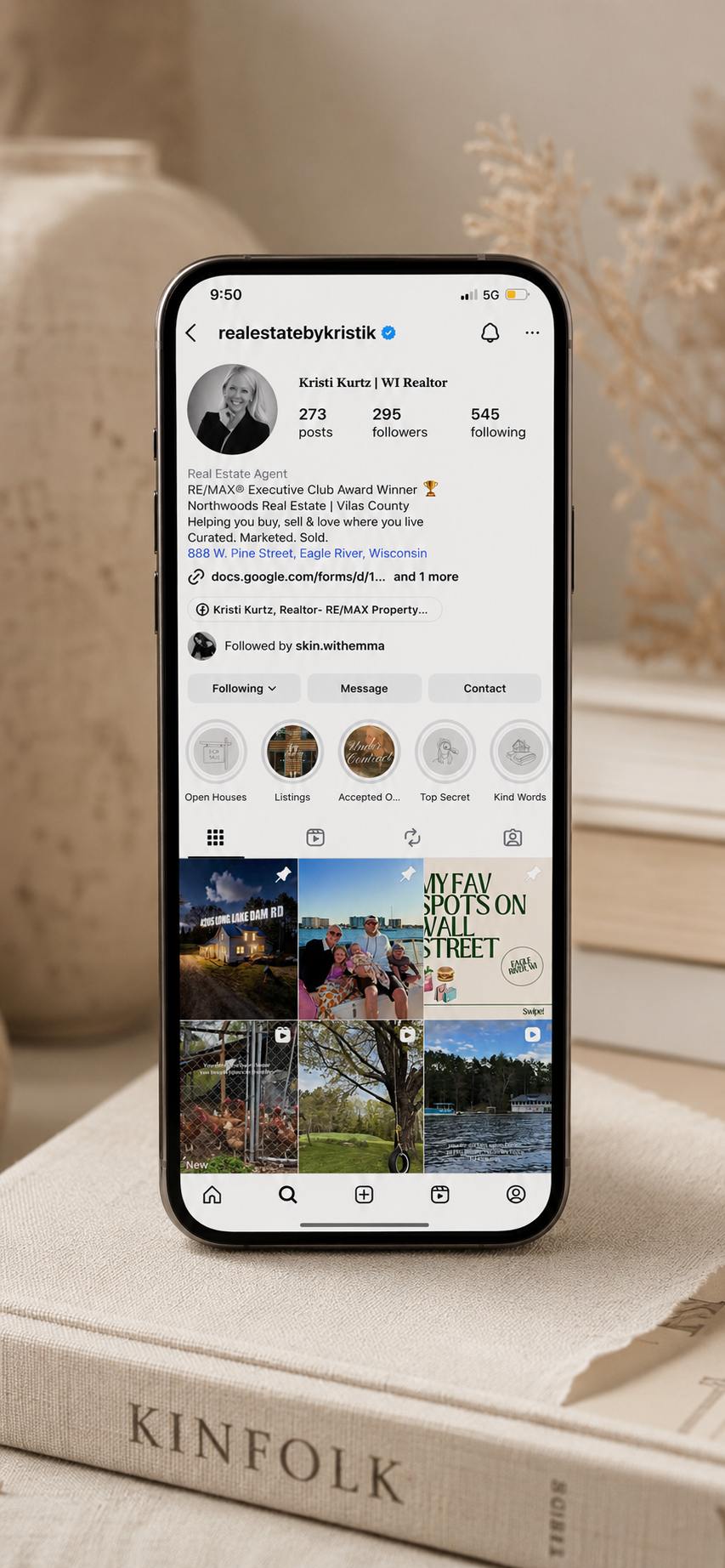 iPhone displaying Instagram profile of Kristi Kurtz, a real estate agent, with profile details and posts, placed on a beige book titled 'Kinfolk' with decorative vases in the background.