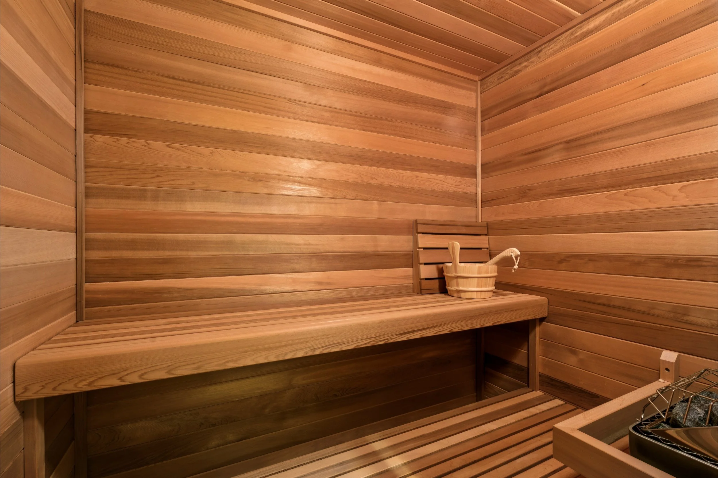Inside a wooden sauna with wooden bench seating and a small wooden bucket on the bench.