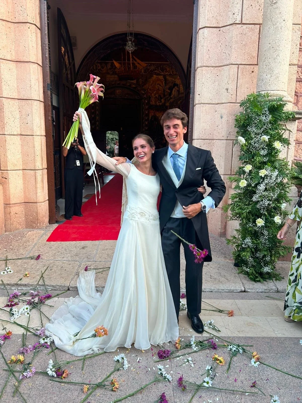 Pareja de recién casados feliz en la entrada de una iglesia, rodeados de flores, celebrando su boda.
