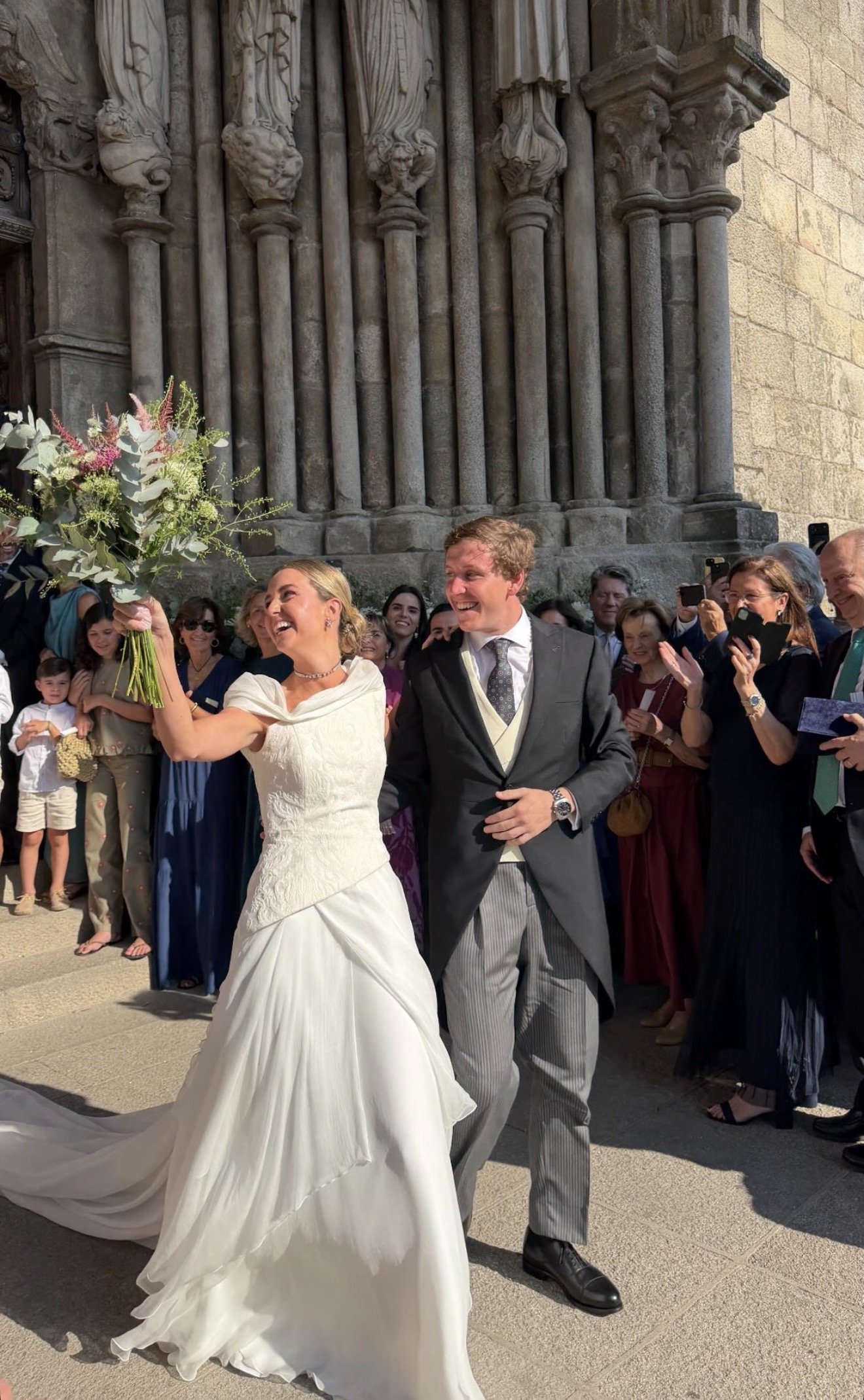 Novios a la salida de la iglesia alzando el ramo de novia silvestre.