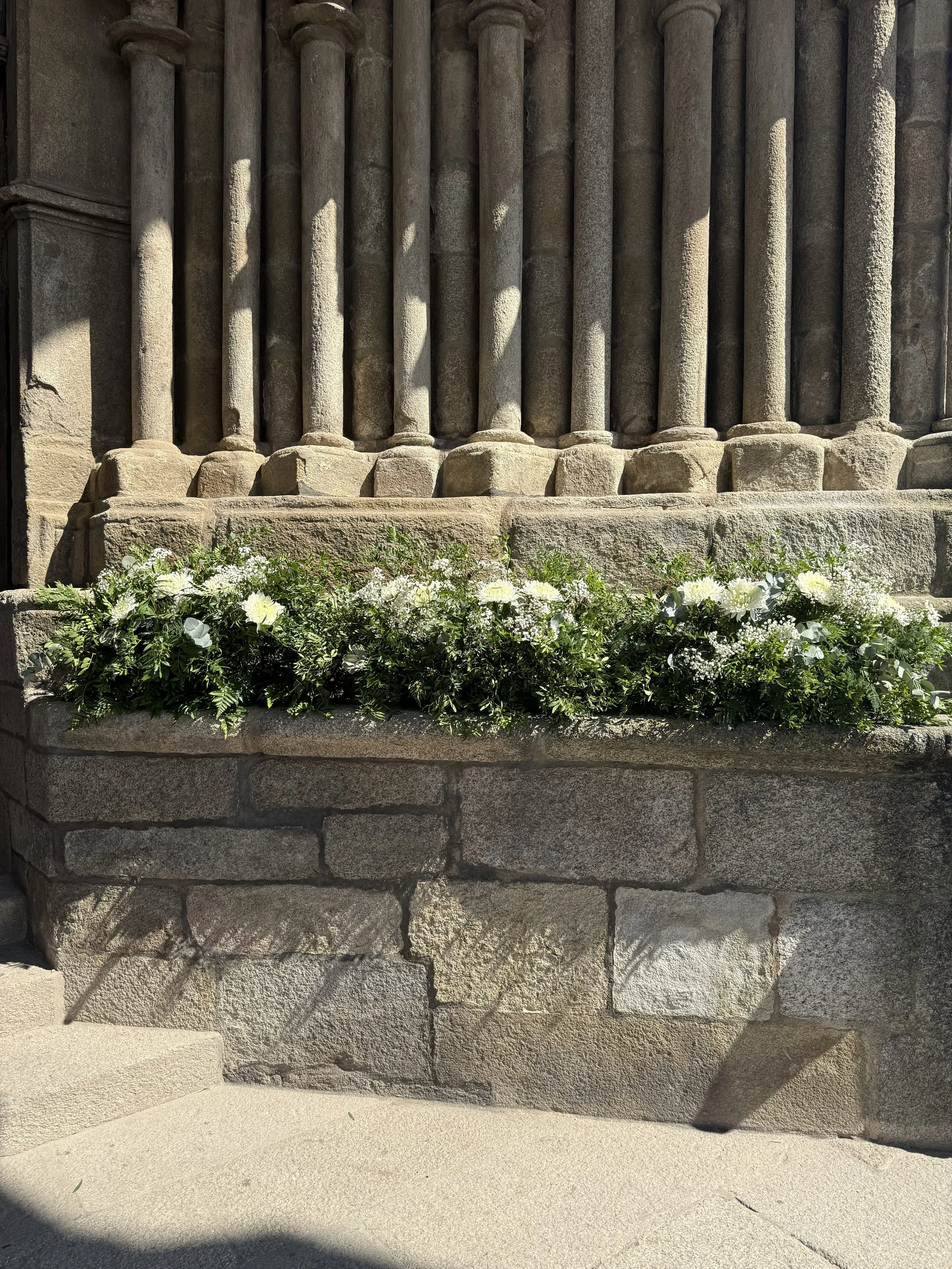 Muros de piedra con columnas y flores blancas en la base