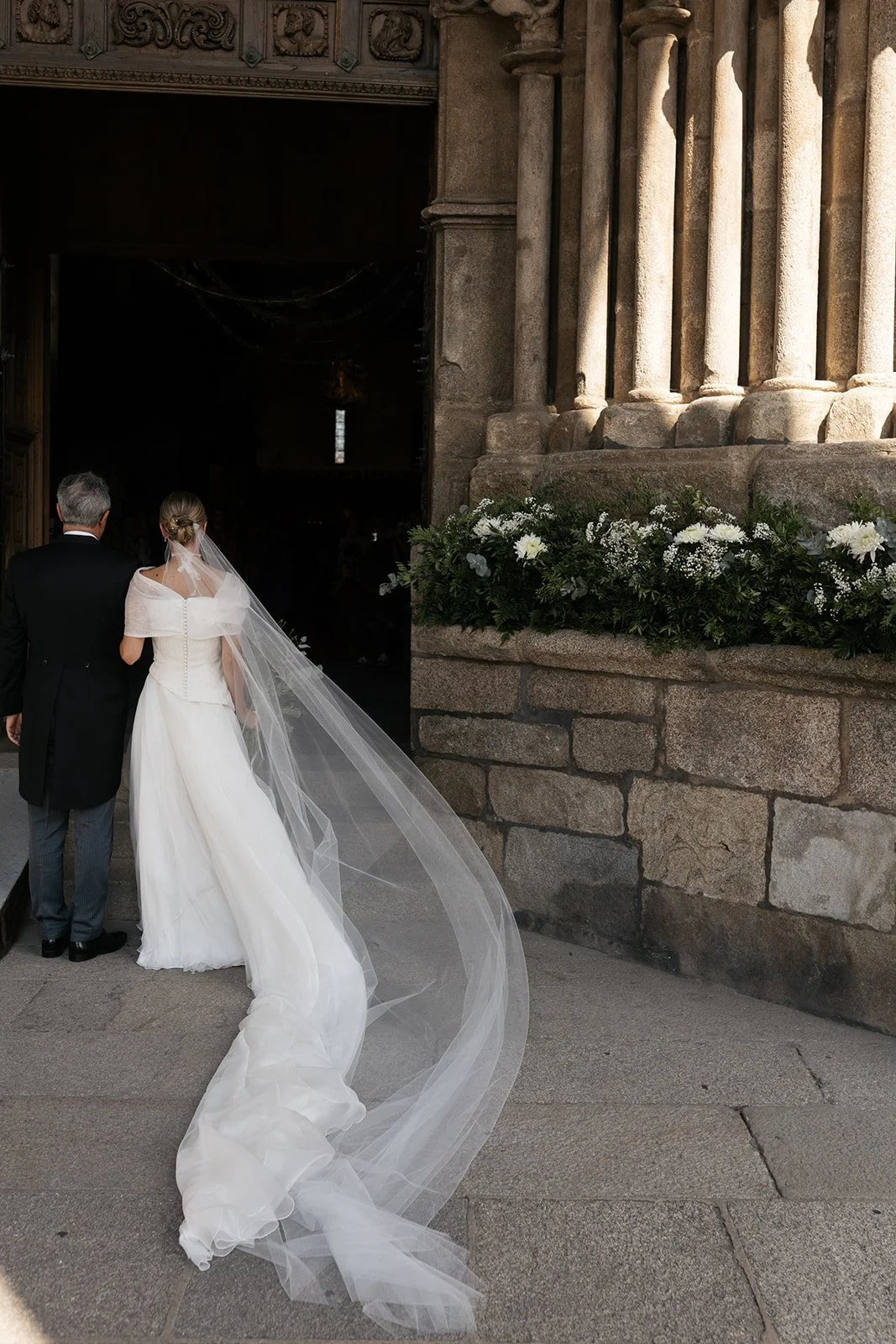 Entrada de la novia a la iglesia, con la decoración floral de la puerta.