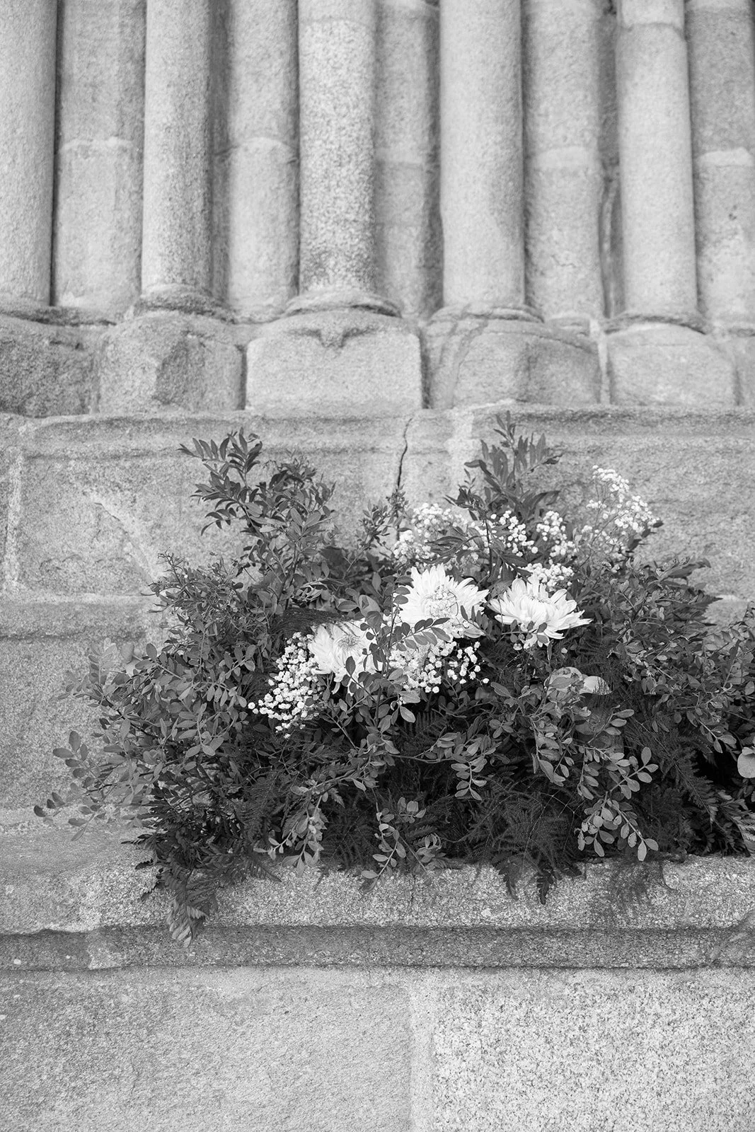 Jarrón de flores en una base de piedra, frente a una pared de columnas de piedra.