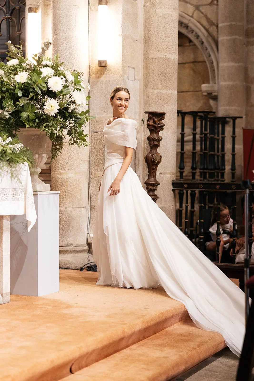 Novia en la iglesia junto a los pedestales de la decoración floral.